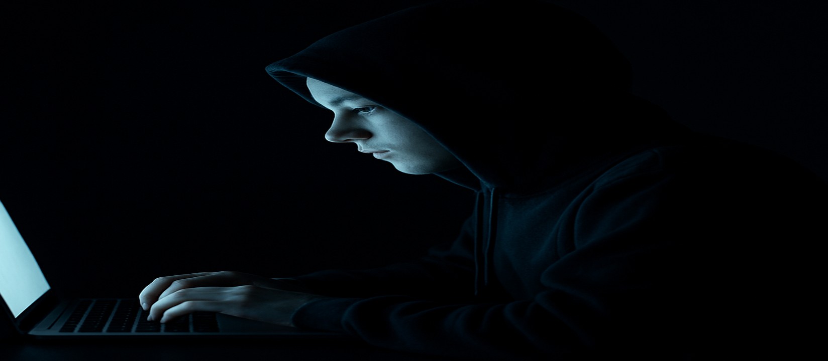 একজন ব্যক্তি অন্ধকার ঘরে ল্যাপটপের সামনে মনোযোগ দিয়ে abc77 ওয়েবসাইটে অনলাইন গেমিং করছেন